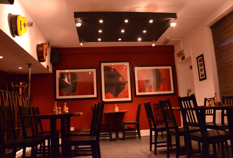 The dining room at La Vaca — oxblood walls, dark timber tables, guitars on the wall